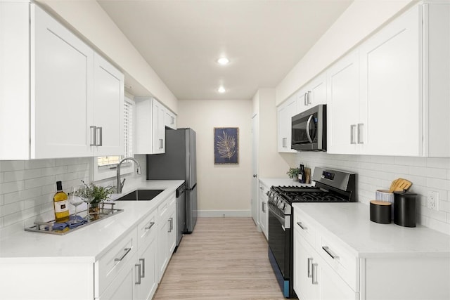 kitchen with baseboards, white cabinets, stainless steel appliances, light countertops, and a sink