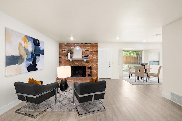 living area with a brick fireplace, visible vents, baseboards, and wood finished floors