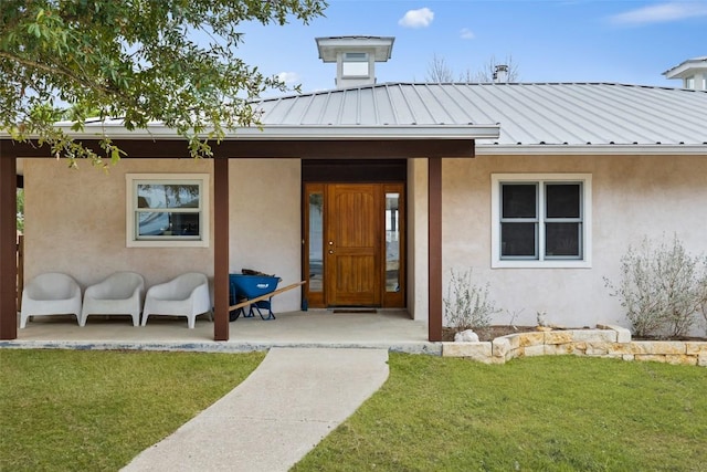 entrance to property with stucco siding, a lawn, and a standing seam roof