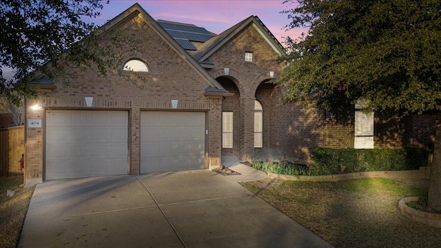 view of front facade with a garage, concrete driveway, solar panels, and brick siding