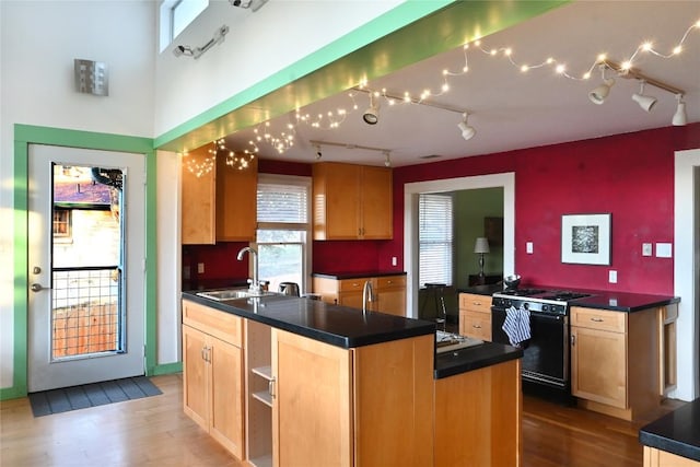 kitchen with wood finished floors, a sink, light brown cabinetry, gas range oven, and dark countertops