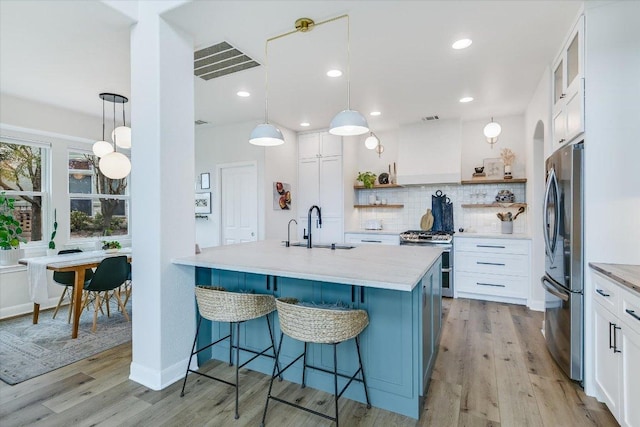 kitchen with visible vents, stainless steel appliances, wall chimney range hood, open shelves, and a sink