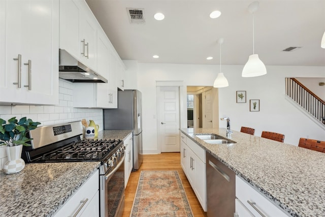 kitchen with stainless steel appliances, visible vents, a sink, light wood-type flooring, and under cabinet range hood