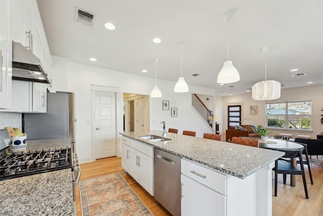 kitchen featuring white cabinets, stainless steel appliances, light wood-type flooring, under cabinet range hood, and a sink