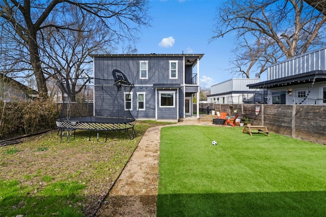 back of property featuring a yard, a trampoline, a fenced backyard, and a balcony