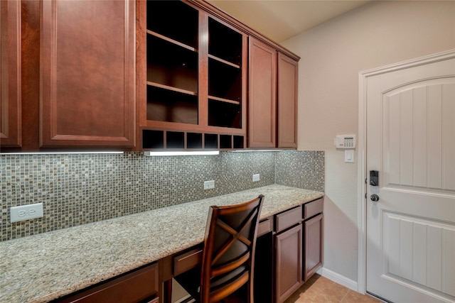 kitchen featuring light tile patterned floors, baseboards, light stone countertops, tasteful backsplash, and built in desk