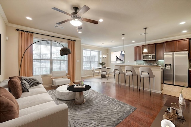 living room featuring recessed lighting, ceiling fan with notable chandelier, visible vents, light wood-style floors, and ornamental molding