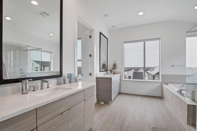 full bath featuring a tub to relax in, two vanities, a sink, and recessed lighting