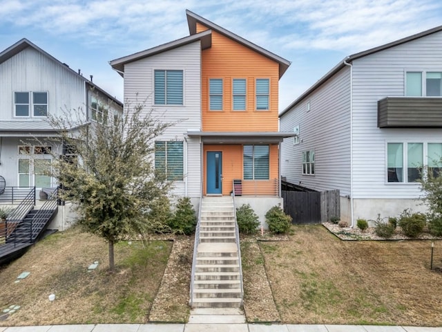 modern home featuring stairs, a front lawn, and fence