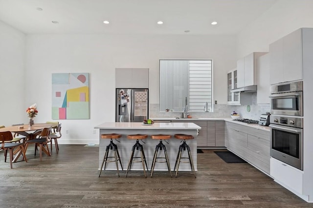 kitchen with appliances with stainless steel finishes, a kitchen island, a sink, modern cabinets, and a kitchen breakfast bar