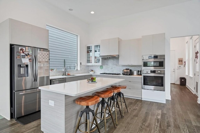 kitchen with appliances with stainless steel finishes, light countertops, dark wood-type flooring, and tasteful backsplash