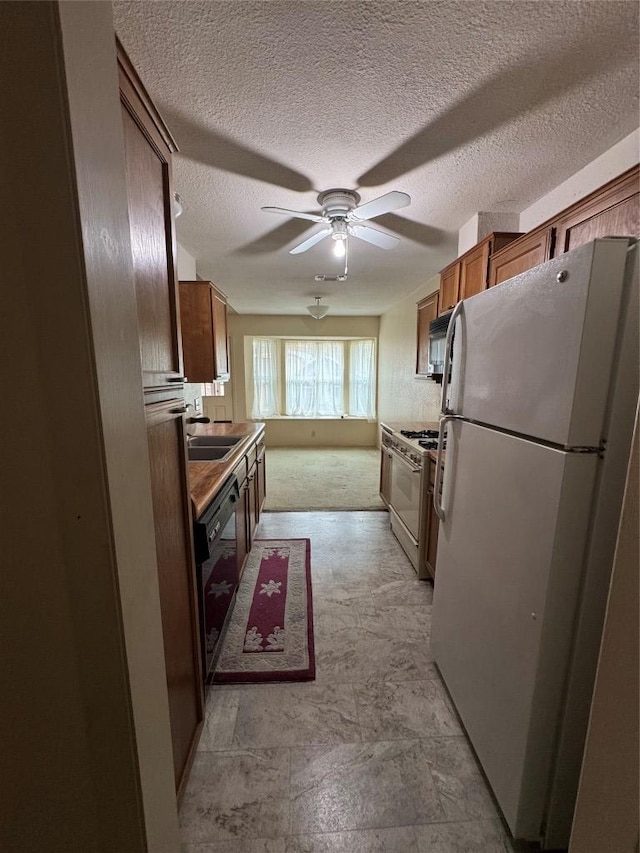 kitchen with ceiling fan, a textured ceiling, white appliances, a sink, and brown cabinets