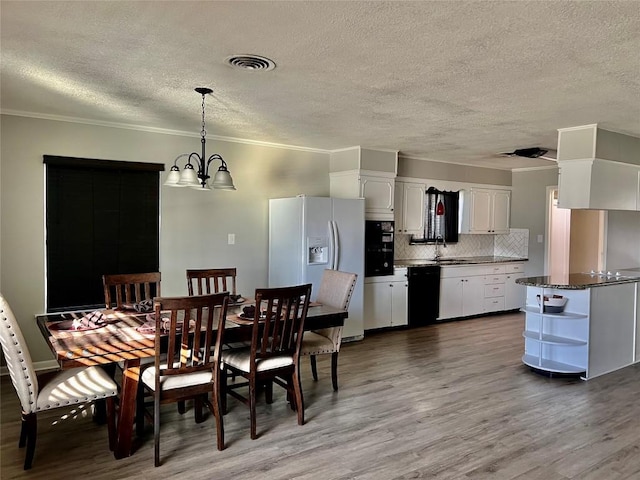 dining room featuring a textured ceiling, a notable chandelier, wood finished floors, visible vents, and ornamental molding