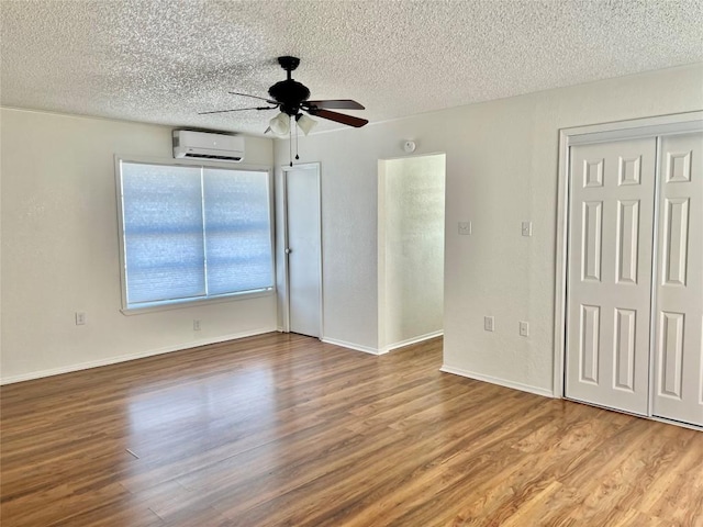 interior space featuring a ceiling fan, a wall mounted air conditioner, a textured ceiling, and wood finished floors