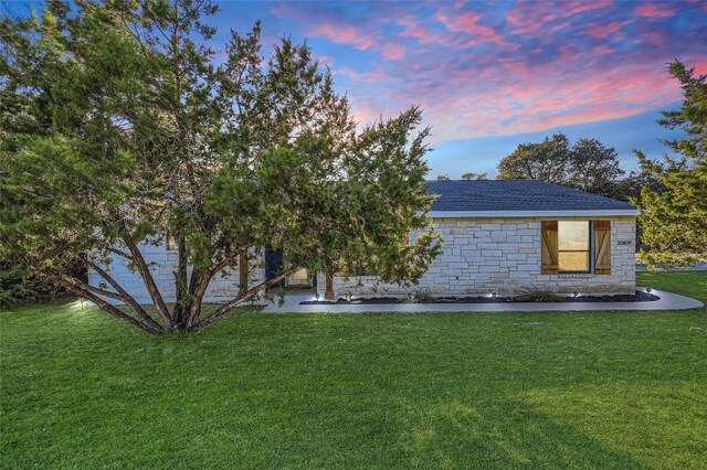 exterior space with a shingled roof, stone siding, and a yard