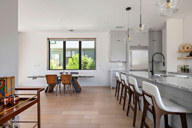 1712 Nash Ave Unit A, Austin, TX 78704 - kitchen featuring stainless steel built in refrigerator, a breakfast bar, decorative light fixtures, light wood-style flooring, and light stone counters
