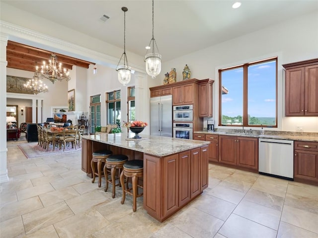 kitchen featuring a notable chandelier, stainless steel appliances, brown cabinetry, and light stone counters