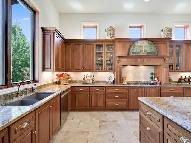 kitchen with brown cabinetry, light stone counters, appliances with stainless steel finishes, and a sink