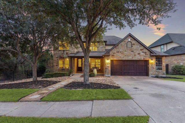 view of front of home featuring stone siding, concrete driveway, an attached garage, and fence