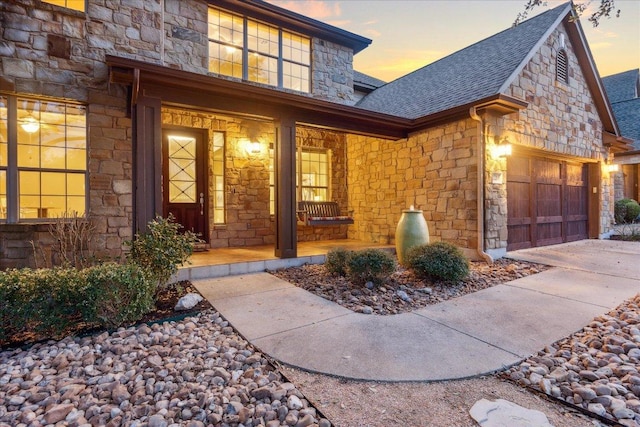 property entrance with a garage, stone siding, a porch, and roof with shingles