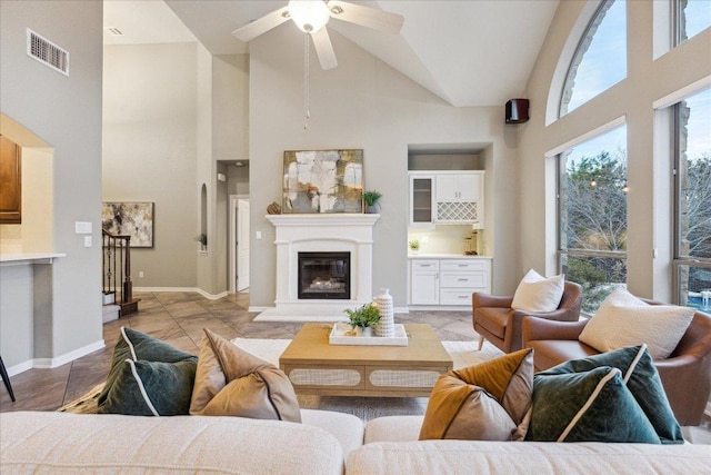 living room featuring visible vents, a ceiling fan, a glass covered fireplace, high vaulted ceiling, and baseboards