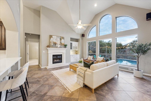 tiled living area featuring a healthy amount of sunlight, ceiling fan, high vaulted ceiling, and a glass covered fireplace