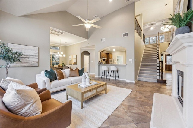 living area with ceiling fan with notable chandelier, a glass covered fireplace, visible vents, and stairs