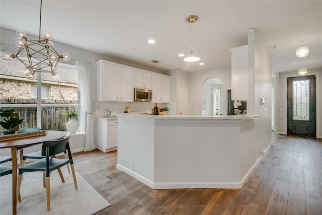 kitchen with arched walkways, stainless steel microwave, light wood-type flooring, and white cabinets