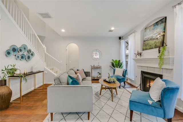 living room with arched walkways, a fireplace, light wood finished floors, visible vents, and stairway