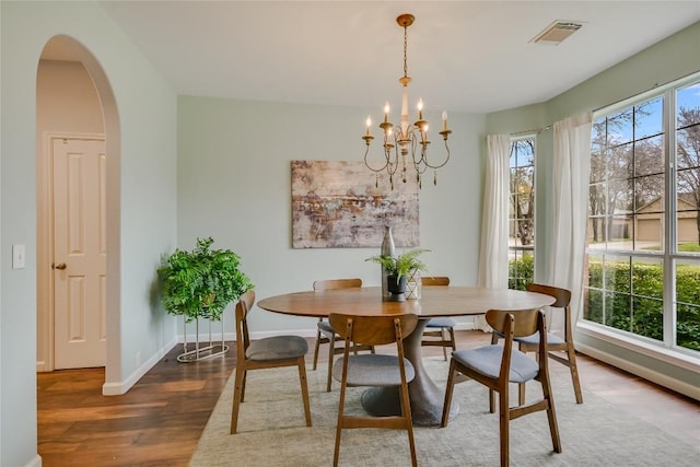 dining space with arched walkways, a chandelier, wood finished floors, visible vents, and baseboards