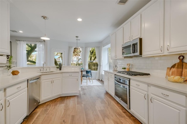 kitchen with decorative backsplash, light wood-style flooring, stainless steel appliances, white cabinetry, and a sink