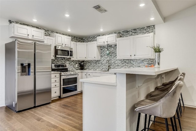 kitchen featuring stainless steel appliances, a breakfast bar, a peninsula, visible vents, and decorative backsplash