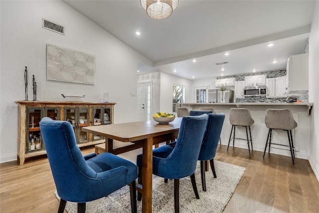 dining room featuring light wood finished floors, baseboards, visible vents, lofted ceiling, and recessed lighting