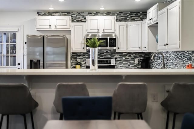 kitchen with appliances with stainless steel finishes, a breakfast bar, light countertops, white cabinetry, and backsplash