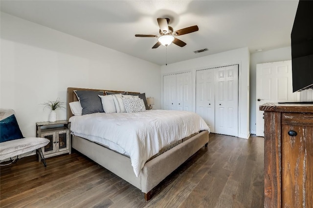 bedroom with multiple closets, dark wood-style flooring, visible vents, and ceiling fan