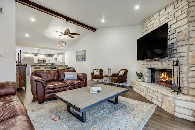living room with visible vents, lofted ceiling with beams, ceiling fan, wood finished floors, and a stone fireplace