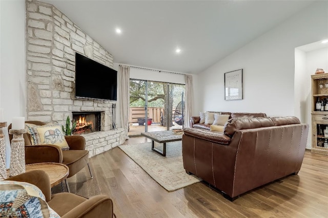 living area featuring lofted ceiling, a stone fireplace, and wood finished floors