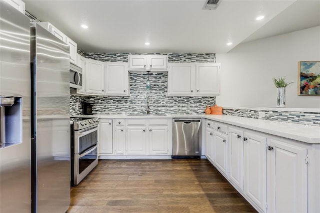 kitchen featuring dark wood finished floors, stainless steel appliances, visible vents, a sink, and a peninsula