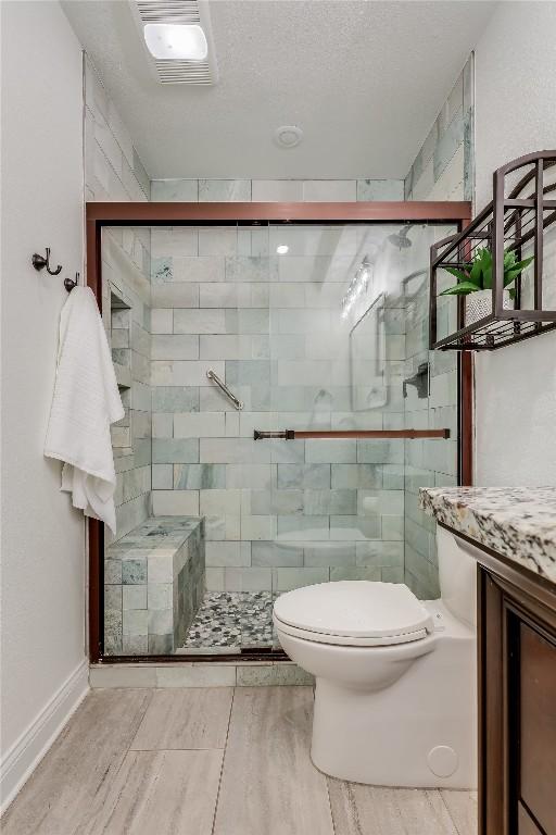 full bathroom featuring toilet, a stall shower, visible vents, and a textured ceiling