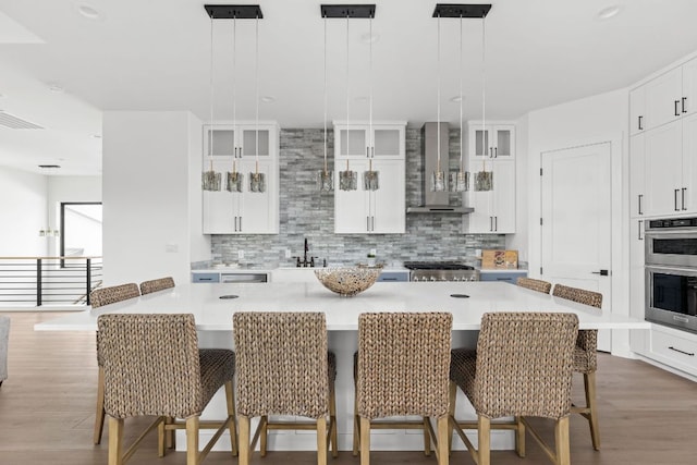 1105 Oak Hurst Rd, Austin, TX 78734 - kitchen with wall chimney exhaust hood, wood finished floors, stainless steel double oven, glass insert cabinets, and decorative backsplash