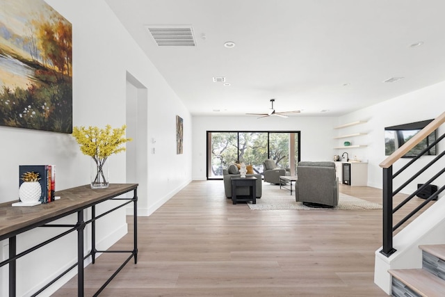 living area featuring light wood-type flooring, visible vents, baseboards, and stairs