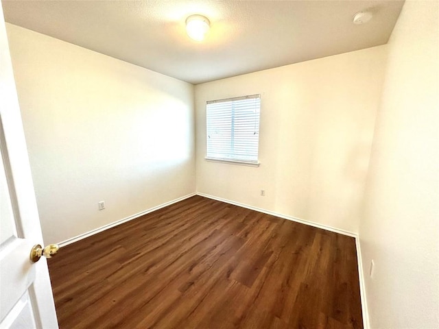 unfurnished room featuring baseboards and dark wood-type flooring