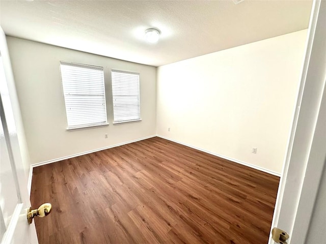 spare room with baseboards and wood finished floors