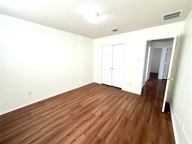 unfurnished bedroom featuring baseboards, a closet, visible vents, and wood finished floors