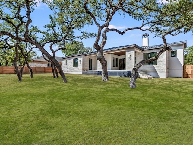 rear view of property with stone siding, metal roof, a standing seam roof, fence, and a yard