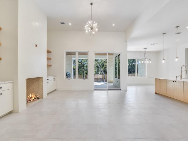 unfurnished living room with a chandelier, a warm lit fireplace, a sink, and visible vents