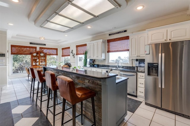 kitchen with stainless steel appliances, ornamental molding, white cabinetry, a kitchen island, and a kitchen breakfast bar