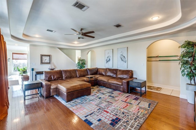 living room featuring a tray ceiling, visible vents, and arched walkways