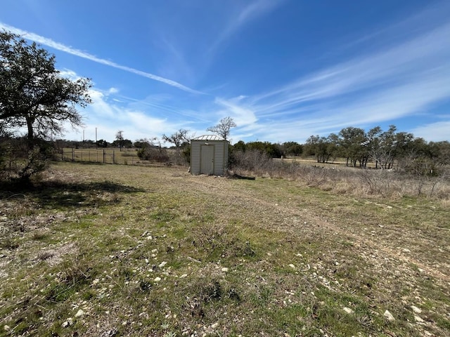 view of yard featuring a rural view, an outdoor structure, fence, and a storage unit