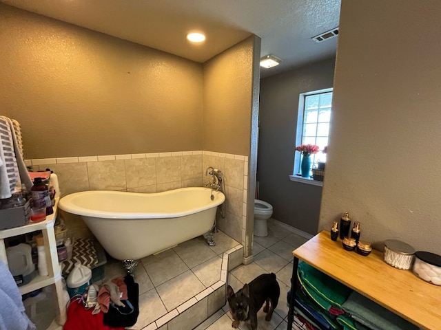 bathroom with toilet, visible vents, tile walls, a soaking tub, and tile patterned floors